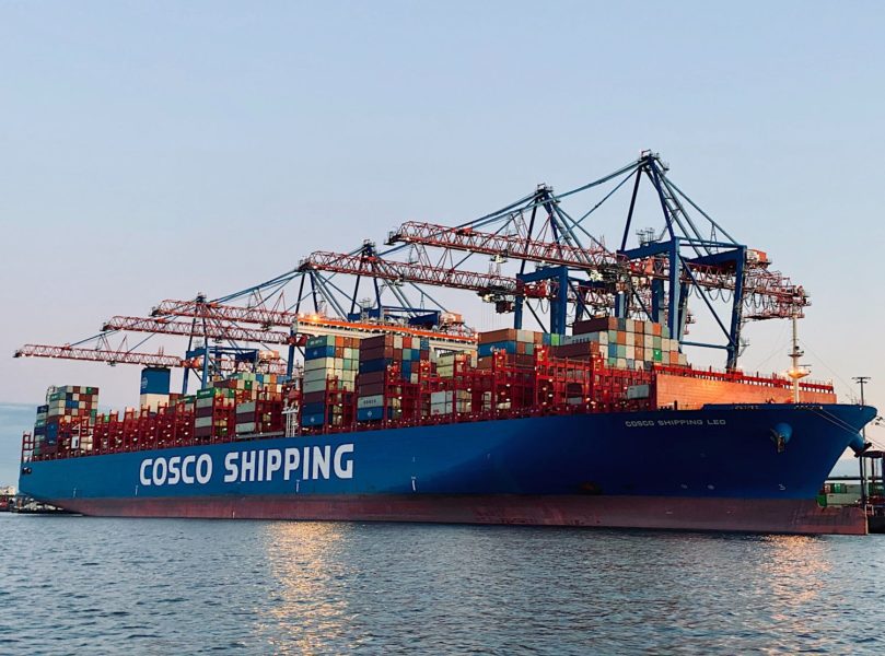 A container ship while being loaded on port. The hull is not fully submerged.